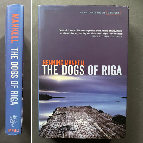 The image shows two views of a book titled 'The Dogs of Riga' by Henning Mankell. The cover features a picture of a dog on a wooden pier with a body of water and a sunset in the background.