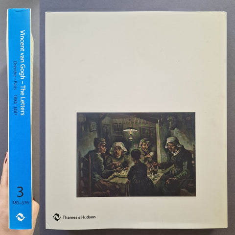 A book titled 'Vincent van Gogh - The Letters' by Davidde Buis, shown with its blue spine on the left and the cream-colored front cover on the right, featuring a painting of Van Gogh's family dinner. A hand is holding the spine on the left edge.