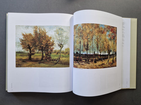 An open art book showing two landscape prints side by side on white pages, photographed from above on a dark gray surface.