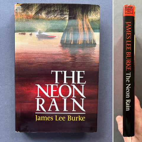 The image shows the cover and the spine of the book titled 'The Neon Rain' by James Lee Burke. The cover features a dark, moody depiction of a tree and water reflecting a neon glow, while the spine displays the title and author's name.