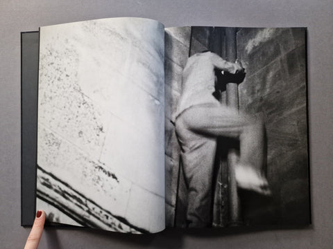 An open black-and-white art book, showing a photographic print of a person climbing or leaning against a wall on the right page.