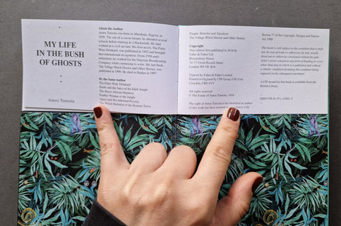 An open book or booklet laid flat on a patterned surface, with a hand holding one page. The left page reads 'MY LIFE IN THE BUSH OF GHOSTS' and the right page contains author and copyright text.