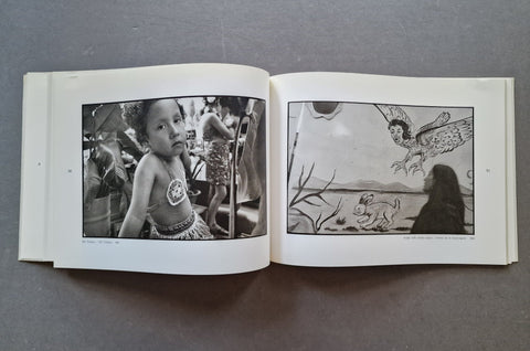 An open book laid flat on a gray surface, showing two black-and-white printed pages with photographs - one of a little girl and the other of a woman passing a mural.