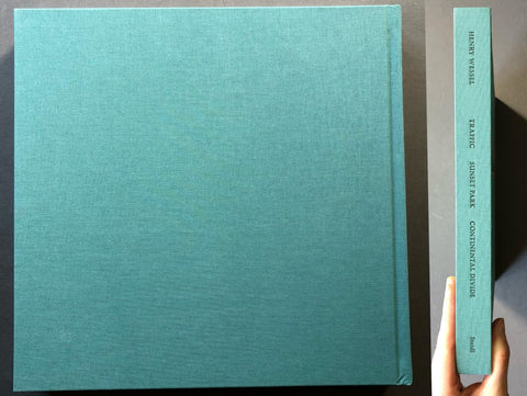 A large hardcover book or photo album with a textured teal-blue cover, shown from the front with its spine visible next to it. A hand is holding the spine to show thickness.
