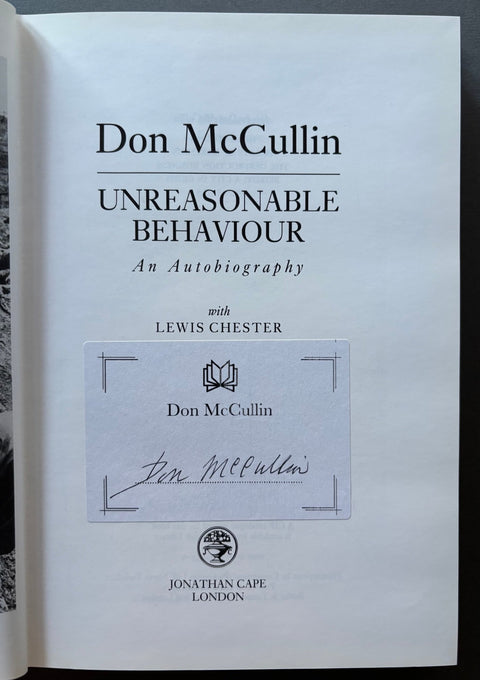 The title page of the book 'Unreasonable Behaviour: An Autobiography' by Don McCullin, featuring a printed white page with black text and a central autograph insert, photographed against a dark background.