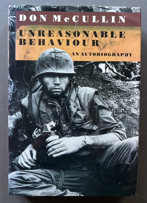 The front cover of the book 'Unreasonable Behaviour: An Autobiography' by Don McCullin, featuring a black and white historical photograph of a World War II soldier wearing a helmet and holding a camera. The title is displayed in bold yellow and white text on a brown and orange banner at the top.
