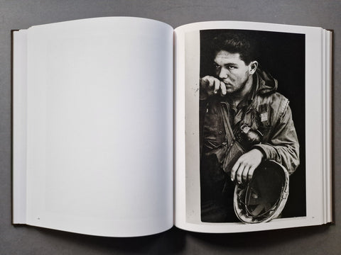 An open book, showing a black-and-white portrait photograph printed on the right page. The left page is blank white, and the photo depicts a man in a jacket holding a helmet.