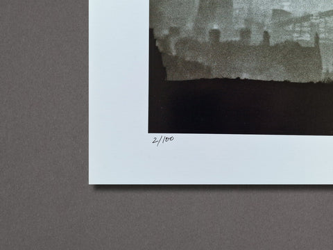 Close-up of a monochrome art print with a wide white border, showing a dark black-and-gray photographic scene and a handwritten edition mark reading 2/100 on the margin.