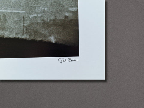A close-up of a signed art print featuring a dark, textured landscape photograph with a wide white border and an artist signature reading 'Jen-Bae' below the image, set against a solid dark gray background.