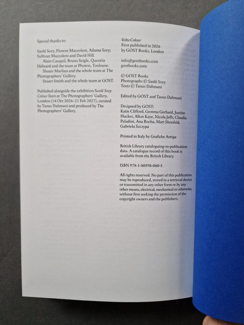 A printed booklet or instruction sheet with black text on white paper, photographed from above against a blue surface with a hand visible at the top right.