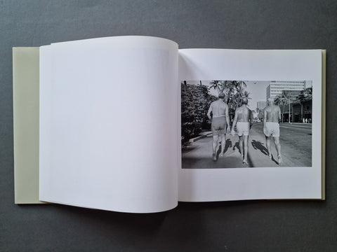 An open hardcover book, showing a black-and-white street photograph printed on the right page with two men walking outdoors.