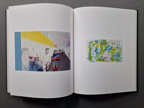 An open book showing two printed pages side by side on a dark gray background. The left page contains a large photograph with a colorful yellow and blue architectural scene, and the right page shows a small abstract artwork in green, pink, and blue.