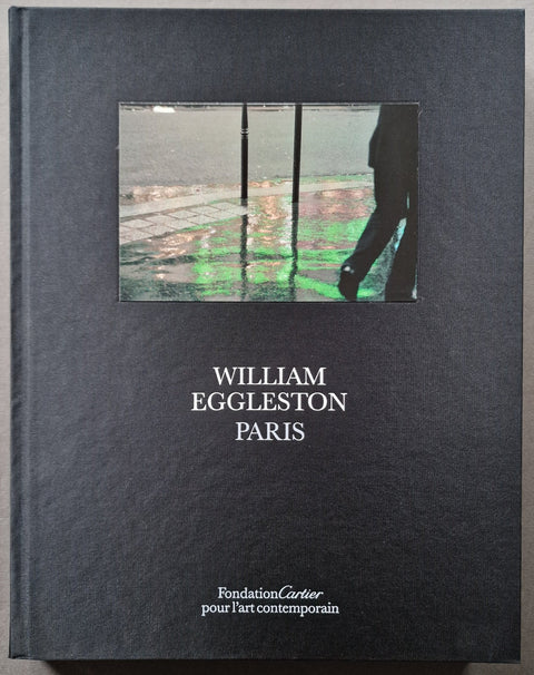 William Eggleston Paris book cover in dark charcoal/black textured material, with a rectangular inset photo near the top showing a figure and green reflections, and white text reading 'WILLIAM EGGLESTON PARIS' and 'Fondation Cartier pour l'art contemporain' near the bottom.