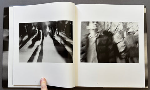 An open book or photo album showing two black-and-white photographic prints on the pages, with a finger holding the bottom edge against a dark surface.
