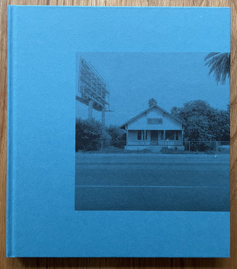 The photography book cover of Seventy Two and One Half Miles Across Los Angeles by Mark Ruwedel. Hardback in blue with image of a house at the side of a road.