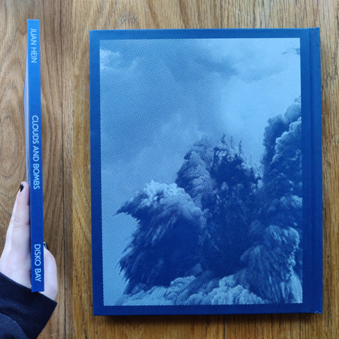 The photography book cover of Clouds and Bombs by Juan Hein. In hardcover blue.