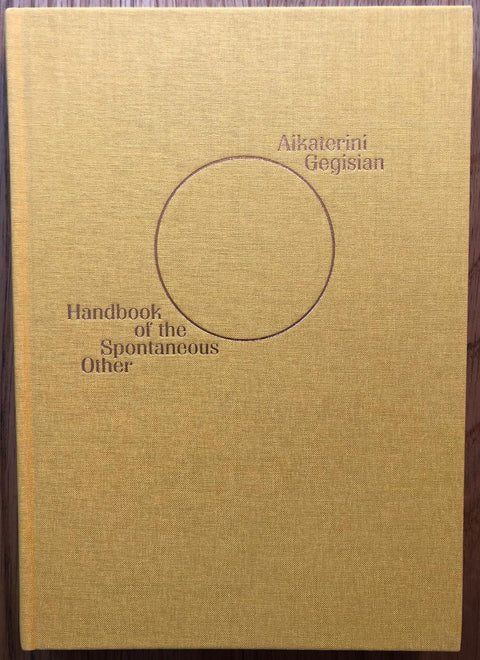 The photography book cover of Handbook of the Spontaneous Other by Aikaterini Gegisian. Hardback in yellow with a circle in the centre. Signed.