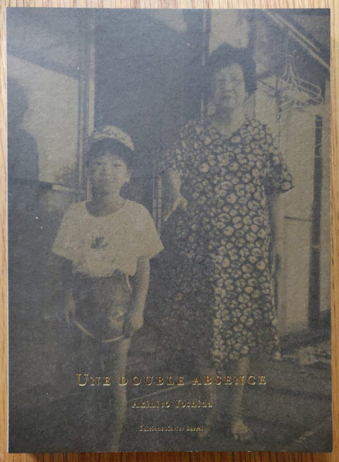 The photography book cover of Une Double Absence by Akihito Yoshida. Paperback with woman and boy on the cover, gold title.