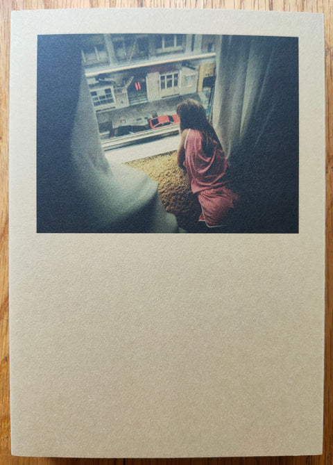 The photography book cover of An Attic Full of Trains by Alberto di Lenardo. Paperback in cream with photo of a girl looking out her window.