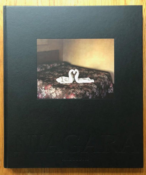 The photography book cover of Niagra by Alec Soth. Hardback in black with a photograph of two towel swans in the shape of a heart on a bed.