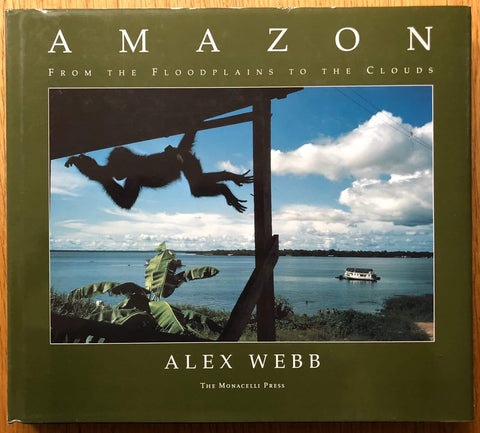 The photography book cover of Amazon: From the Floodplains to the Clouds by Alex Webb. Hardback in dark green with image of a monkey swinging from a banister. In dust jacket.