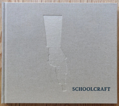 The photography book cover of Schoolcraft by Alice Schoolcraft. Hardback in grey with imprint of a hand holding a gun downwards.
