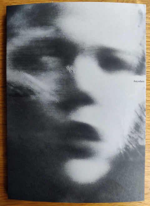 The photography book cover of Anywhere But Here by Alison McCauley. In softcover black and white with a blurred face with french flaps.