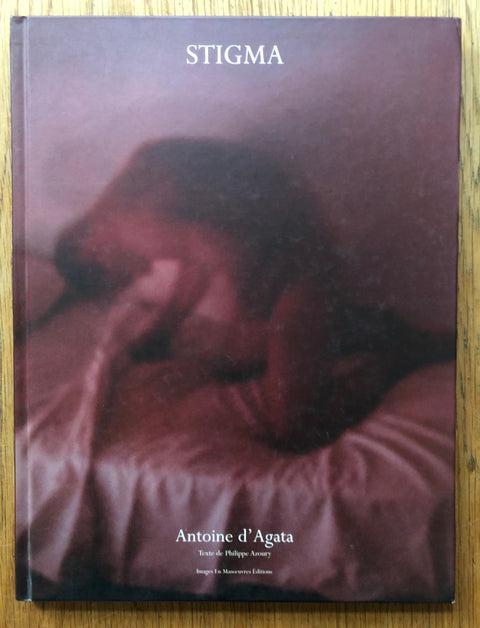 The photography book cover of Stigma by Antoine d'Agata. Hardback in red/purple with hazy image of naked man on bed.