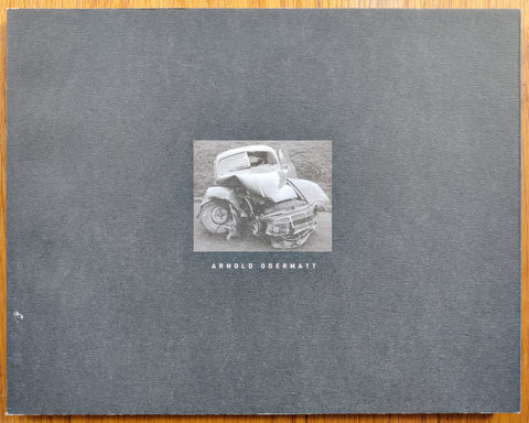 The photography book cover of Arnold Odermatt by Arnold Odermatt. Paperback in dark grey with image of a car wreckage on the cover.