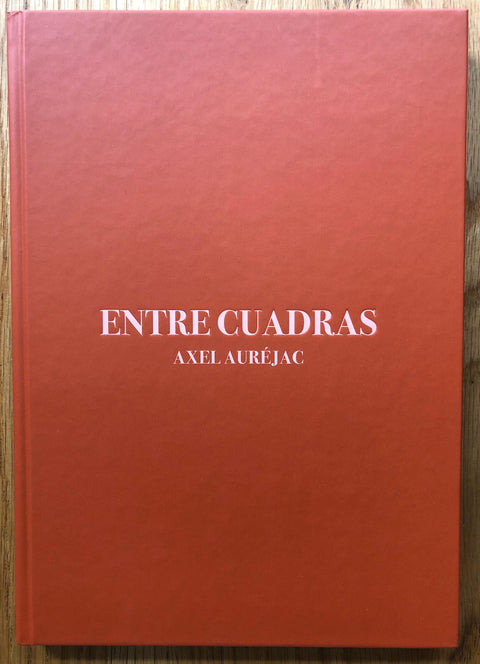The photography book cover of Entre Cuadras by Axel Aurejac. Hardback in red with centred pink title. Signed.