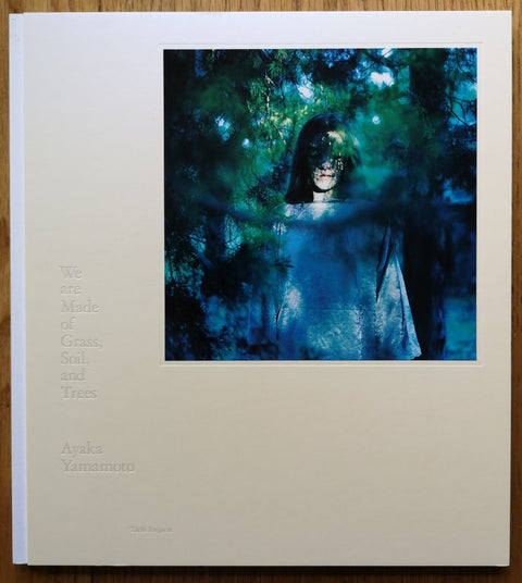 The photography book cover of We are Made of Grass, Soil, and Trees by Ayaka Yamamoto. Hardback with image of a girl standing in the trees.