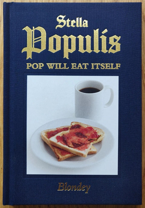 The photography book cover of Stella Populis - Pop Will Eat Itself by Blondey. Hardback in navy blue with gold lettering and photo of toast and coffee in the centre.