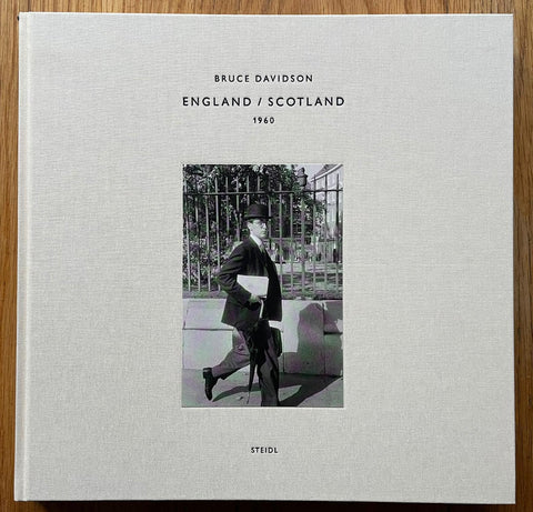 The photography book cover of England / Scotland 1960 by Bruce Davidson. Hardback in white/grey with image of a man walking in a tophat. Signed.