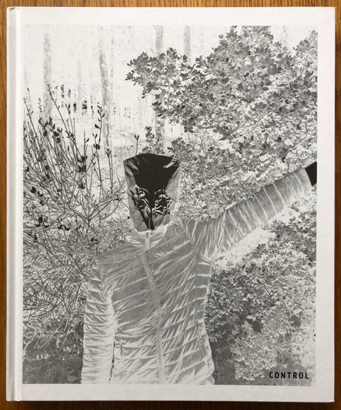 The photography book cover of Control by Cagdas Erdogan. Hardback black and white cover of a masked person in bushes.
