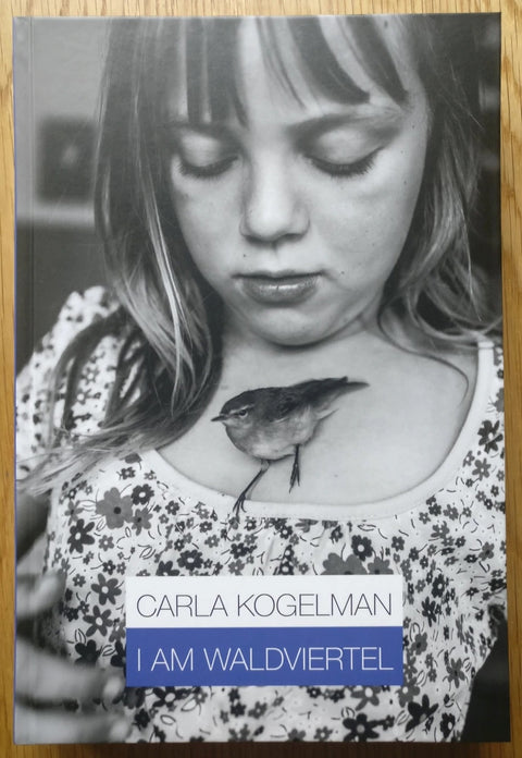 The photography book cover of I am Waldviertel by Carla Kogelman. Hardback with B&W photograph of a girl with a bird perched on her.