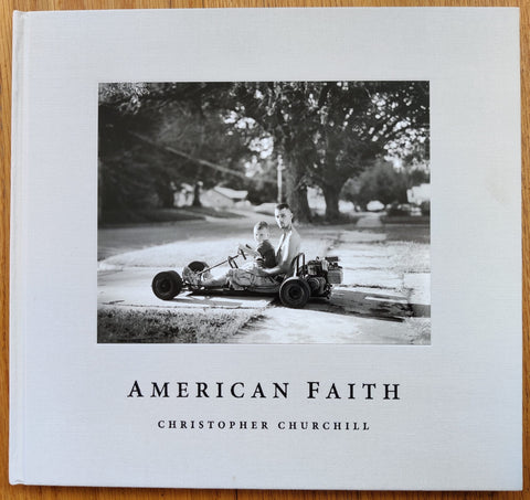 The photography book cover of American Faith by Christopher Churchill. Hardback in white with image of a man and boy in a race car