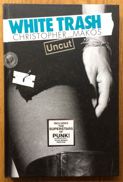 The photography book cover of White Trash Uncut by Christopher Makos. Hardback black and white with blue writing.