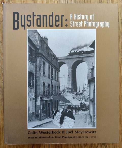 The photobook cover of Bystander: A History of Street Photography by Joel Meyerowitz and  Colin Westerbeck. In softcover brown.