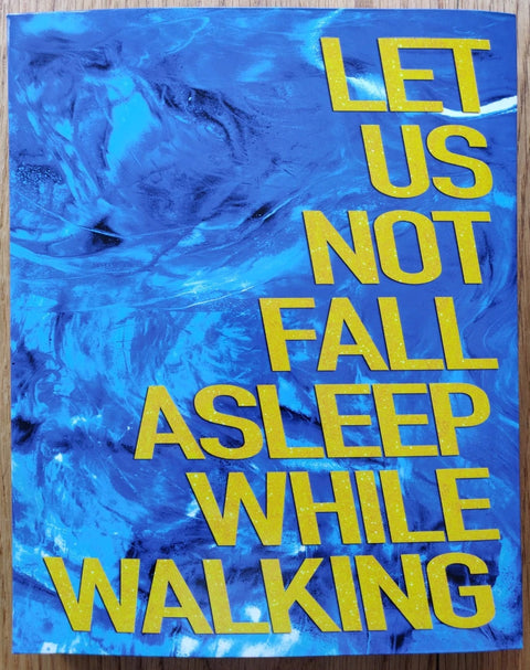 The photography book cover of Let Us Not Fall Asleep While Walking by Daniel Denil. Paperback in blue with yellow writing.
