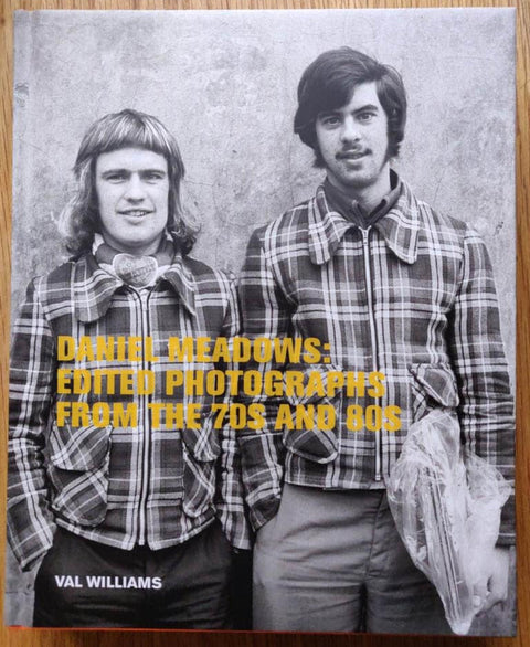 The photography book cover of Daniel Meadows: Edited Photographs from the 70s and 80s. Hardback in B&W with image of two men in chequered shirts on the cover. Title in Yellow.