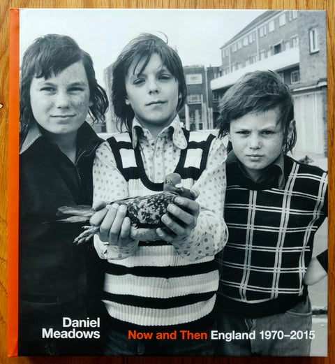 The photography book cover of Now and Then: England 1970-2015 by Daniel Meadows. Hardback with image of three children, the middl eone holding a pigeon.