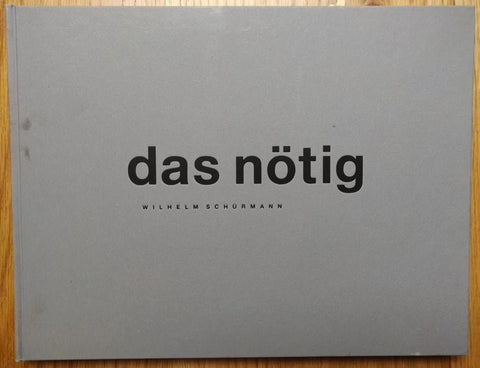 The photography book cover of das nötig by Wilhelm Schurmann. Hardback in grey with large black centred text.
