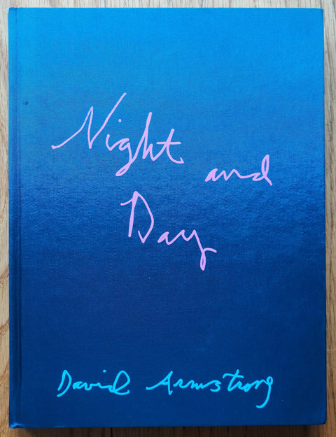 The photography book cover of Night and Day by David Armstrong. Hardback in blue with pink handwriting for the title. Signed.