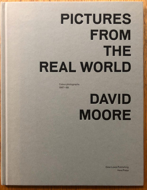 The photography book cover of Pictures from the Real World by David Moore. Hardback in grey/white with large black title.