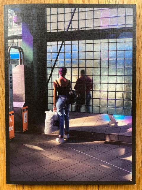 The photography book cover of Roosevelt Station by David Rothenberg. Paperback with image of woman n a station holding an M&S plastic bag