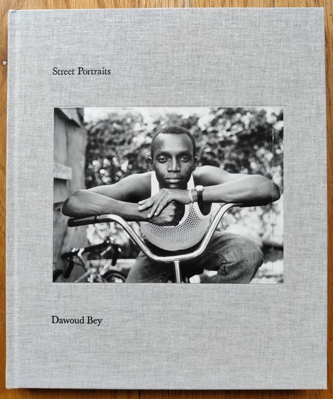 The photography book cover of Street Portraits by Dawoud Bey. Hardback in light grey with a man leaning on his bike handles.