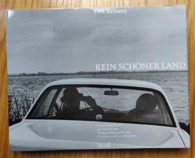 The photography book cover Kein Schoner Land by Dirk Reinartz. Hardback in B&W with a car looking out to a body of water.