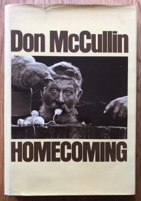 The photography book cover of Homecoming by Don McCullin. Hardback in white with centred B&W image of a man eating a mouse.