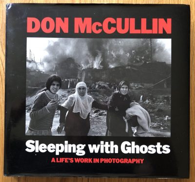 The photography book cover of Sleeping with Ghosts by Don McCullin. Hardback black cover with red and white text.