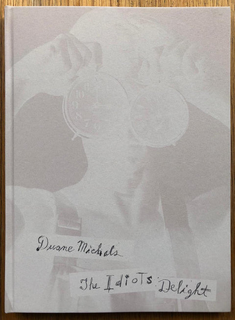The photography book cover of The Idiots of Delight by Duane Michals. Hardback with faded image of someone holding up two clocks to their eyes.